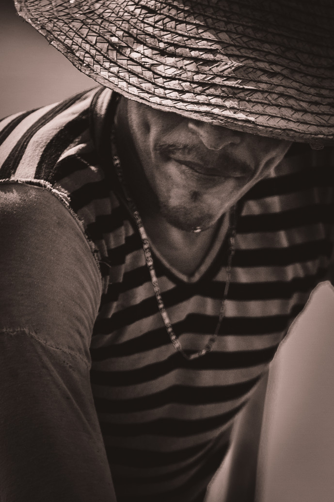 Man smiling under woven hat.